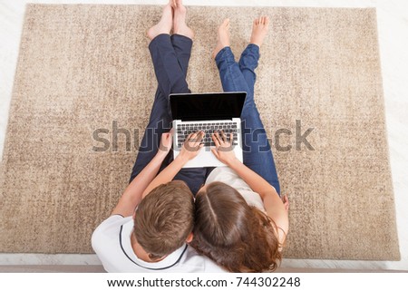 Young couple web surfing on laptop sitting on sofa at home, relaxing, copy space, top view
