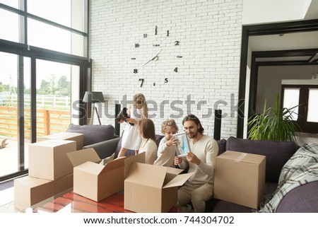 Young happy family with kids unpacking boxes together sitting on sofa in modern living room of country house moving settling in new home, children helping parents to pack stuff move out relocating  Royalty-Free Stock Photo #744304702