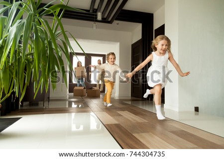 Happy young family with cardboard boxes in new home at moving day concept, excited children running into big modern own house hallway, parents with belongings at background, mortgage loan, relocation 