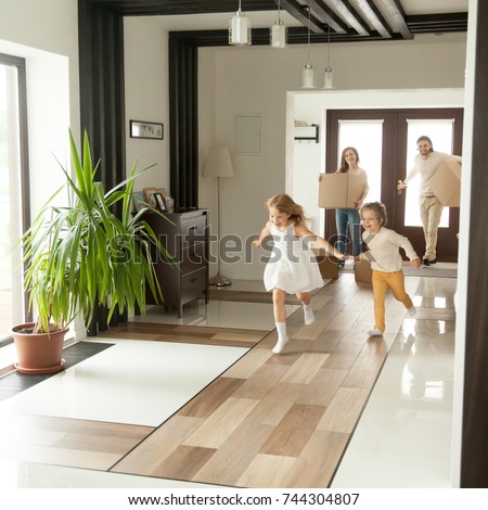Playful happy kids running into new big own beautiful house, family moving in day concept, excited children exploring home interior having fun together, parents holding cardboard boxes at background  Royalty-Free Stock Photo #744304807