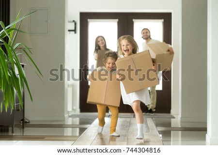 Happy family with kids bought new home, excited children funny girl and boy holding boxes running into big modern house, helping parents with belongings, moving day concept, mortgage and relocation  Royalty-Free Stock Photo #744304816