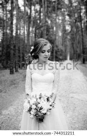 Wedding in the forest. Portrait of a bride in a white dress with a stylish bouquet. Black and white photo