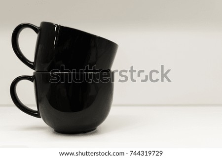 Two mugs on a white background are standing. A black and white mug is next on the table.