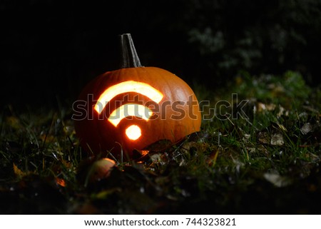 Closeup photo of pumpkin with carved Wi-Fi signal during Halloween night. Shot in garden with fallen apples, grass and leaves during autumn time. Royalty-Free Stock Photo #744323821