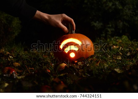 Hand reaching for pumpkin with carved Wi-Fi signal. Halloween night. Shot in garden with fallen apples, grass and leaves. Closeup macro photography during autumn time Royalty-Free Stock Photo #744324151