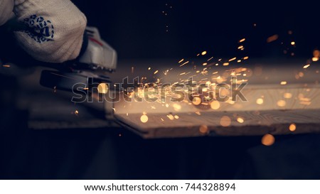 Man cut down the pin in wooden plank with lighting and cords using circular saw. Sparkles all over the place. Man at handmade diy work