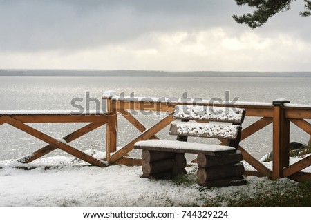 Park wooden bench on the bank of the river, covered with heavy snow. Winter landscape.
