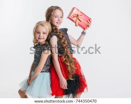Portrait of little girls with curly hairstyle standing on the holiday party in dress with sequins, holding present. Concept Celebration. Christmas. New Year