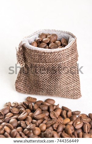 Pile of coffee beans and jute drawstring bag on the white background.