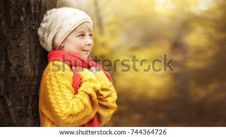  little girl in  yellow sweater and a red scarf lies on  plaid against the backdrop of an autumnal forest and holds a toy plush dog in her hands