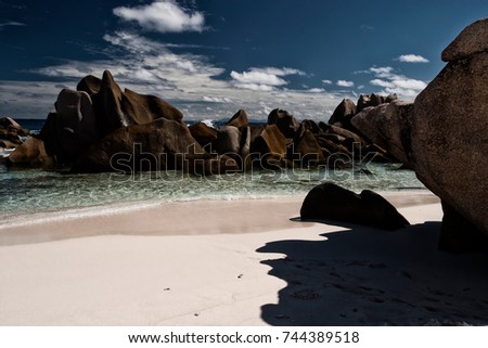 Rocks emerging from the sea in Anse Marron, La Digue, Seychelles pictured from the beach with blue sky and few clouds