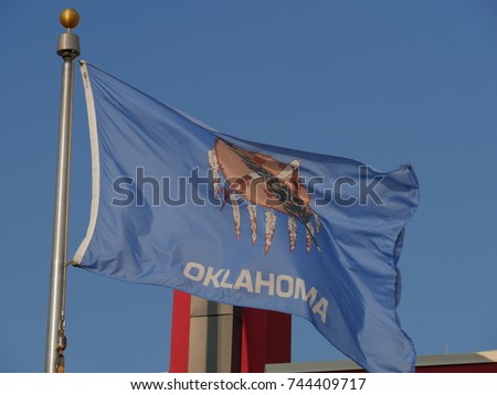 The flag of Oklahoma State flying above a building from a pole