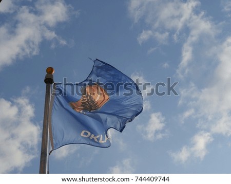 The flag of Oklahoma State fluttering up above clear blue skies from a pole