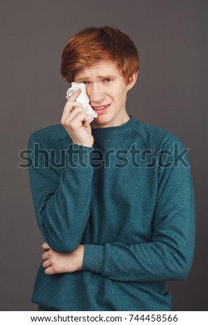 Close up vertical portrait of dramatical ginger good-looking teenager in green sweater holding napkin in hand, wipes up fake tears from face, trying to make friends feeling guilty about abusing him