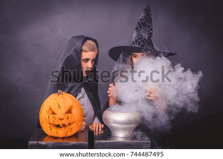 funny girl with a boy in a witch costume for Halloween with pumpkin Jack on a dark background with smoke