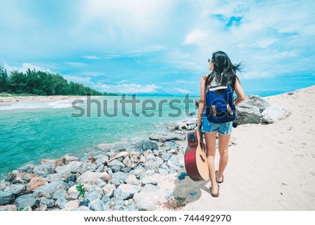 woman traveler standing and happy on the beach. lady holding a guitar at the sea and relaxing on her vacation.