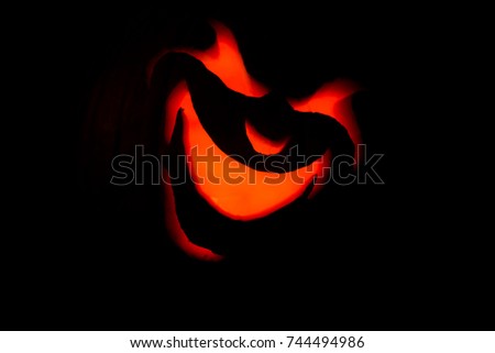 Front close up view of angry jack-o-lantern face lit up by candle and pumpkin blacked out glowing red evil smile 