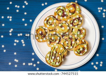 Creative homemade cake made from yeast dough stuffed with cranberries and walnuts with icing and sugar snowflakes. Original festive cake in form of Christmas tree, snowflakes on blue wooden table