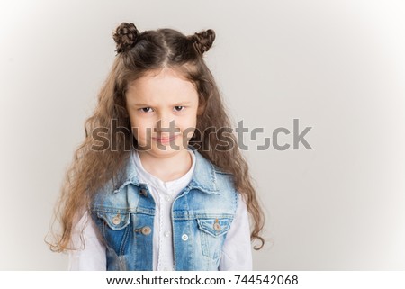 Small girl with blond pony-tail looking seriously, folding hands and frowning eyebrows. Her gloomy appearance says she is very unhappy and offended. Blond baby showing disapproval with pursed lips Royalty-Free Stock Photo #744542068