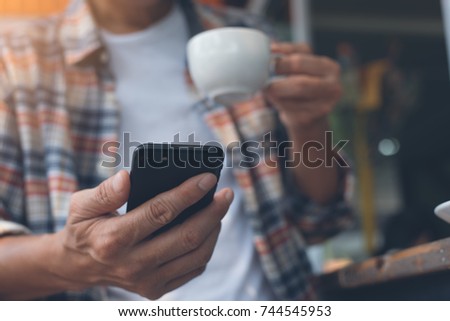 Casual man, hipster using mobile smartphone, drinking coffee in coffee shop.  Man checking internet application or chatting on phone at cafe,  social media, wireless network communication, close up