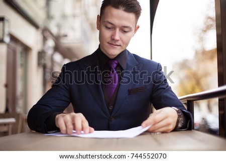 A young man in a suit reads a document before signing the contract.