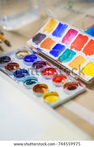 Top view from above on a palette of watercolors prepared by the artist for drawing. Brushes and necessary accessories. School of Art and Drawing Lessons. Soft focus and beautiful bokeh.