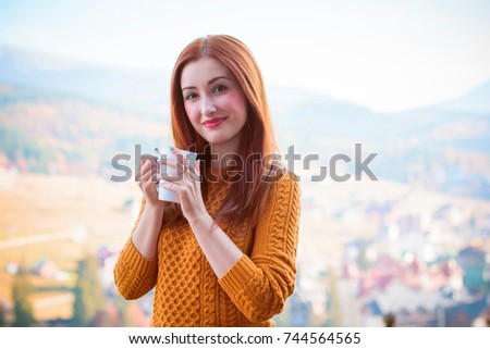 Cute and nice young woman drinking coffee at terrace on a sunny morning in mountain. Pretty lady in stylish casual yellow sweater and shorts. Warm soft cozy image, breakfast on the balcony  