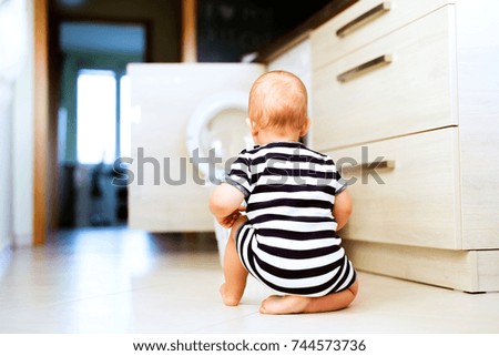 Baby boy by the washing mashine in the kitchen.
