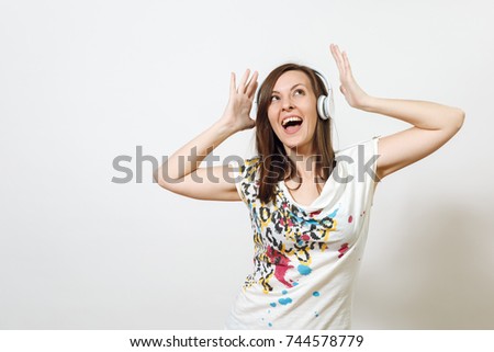 The beautiful emotional European young happy brown-haired woman with healthy clean skin and charming smile, dressed in casual light clothes, listens enjoys music on headphones on a white background.