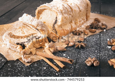 Sliced pound cake with nuts - Delicious dessert on baking paper, a sponge cake filled with poppy seeds and roasted walnuts and almonds, covered with powdered sugar, on a black wooden table