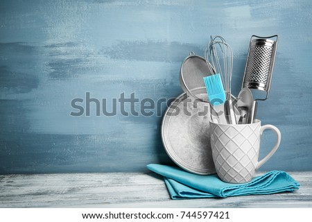 Kitchen utensils in cup on table against wall Royalty-Free Stock Photo #744597421