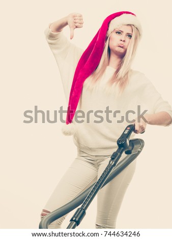 Woman vacuuming the house. Funny teen girl in santa helper hat with vacuum cleaner giving thumb down hand sign gesture. Christmas time and housework concept. Toned image