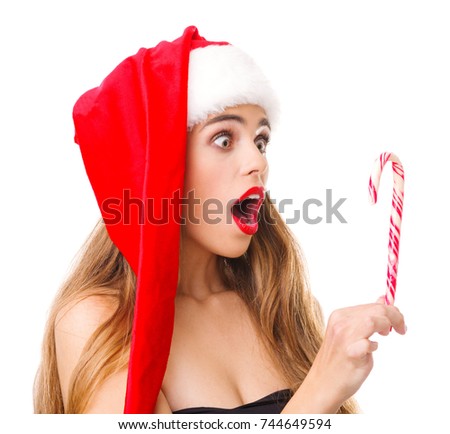 The girl in Santa's cap looks at the lollipop with a surprised look.