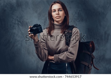 A woman with backpack holds compact photo camera.