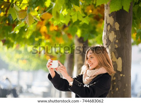 Girl taking photo with mobile phone during autumn in the city