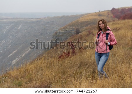 A cute pretty smiling woman with a backpack walking at countryside on autumn misty day.