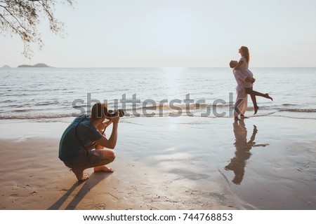wedding and lifestyle photographer taking photos of affectionate couple on the beach at sunset