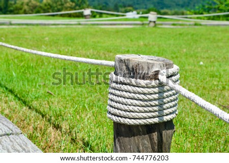 Rope wrapped around a wooden pole in blurred green field.