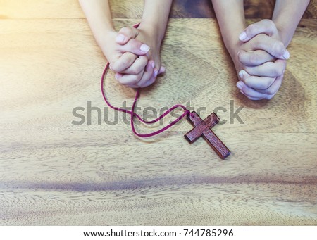Two kids are praying to God together with wooden cross  on wooden table. copy space.