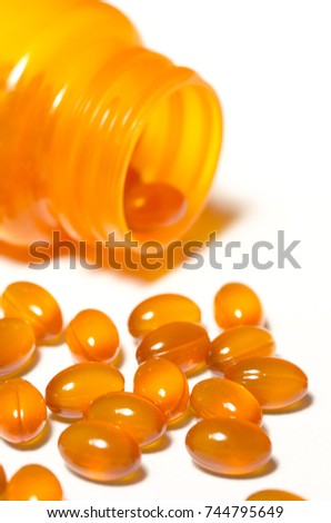 A bottle of orange translucent vitamin pills has been almost emptied onto a white backdrop.  The focus is on the pills in the foreground.