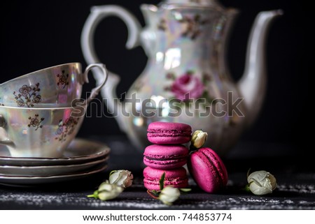 Set of berry macaroons with white roses and a tea-set on dark wooden background. Berry macaroons