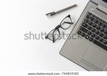 white desk table with office supplies notebook computer and eyeglasses, top view, over light and  soft-focus in the background