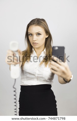 The beautiful girl holds two phones. Beautiful girl in a business suit on a white background with two phones. Different emotions on the face when talking on the phone