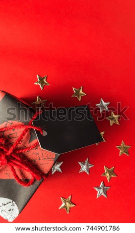 Gift box with empty tag and decoration stars on red background, view from above