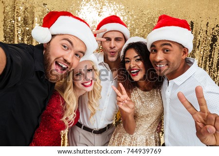 Portrait of a smiling young multiracial group of friends celebrating New Year together while standing and taking a selfie isolated over golden shiny background