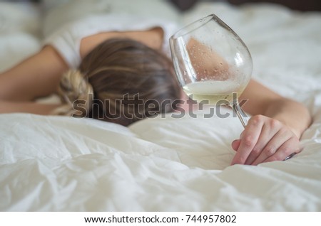 Great concept of alcohol abuse. Young woman, blond hair, fainted in bed after drinking too much alcohol. Glass of wine in hand, bottle of wine. Royalty-Free Stock Photo #744957802