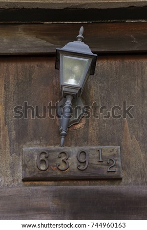 Old house number sign on wooden door with metal overhead lantern, a vertical picture