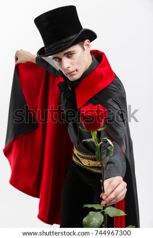 Vampire Halloween Concept - Portrait of handsome caucasian Vampire holding red beautiful rose on white studio background. 