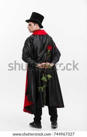 Vampire Halloween Concept - Portrait of handsome caucasian Vampire holding red beautiful rose on white studio background. 