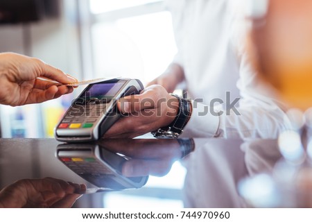 Hand of customer paying with contactless credit card with NFC technology. Bartender with a credit card reader machine at bar counter with female holding credit card. Focus on hands. Royalty-Free Stock Photo #744970960